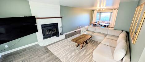 A living room with a fireplace, a sectional sofa, a coffee table, and a flat-screen TV mounted on the wall.
