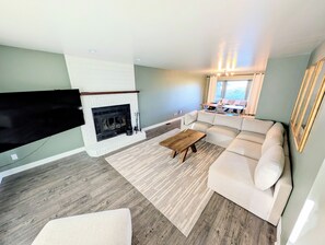 Ett vardagsrum med en öppen spis, en hörnsoffa, ett soffbord och en platt-TV som är monterad på väggen.