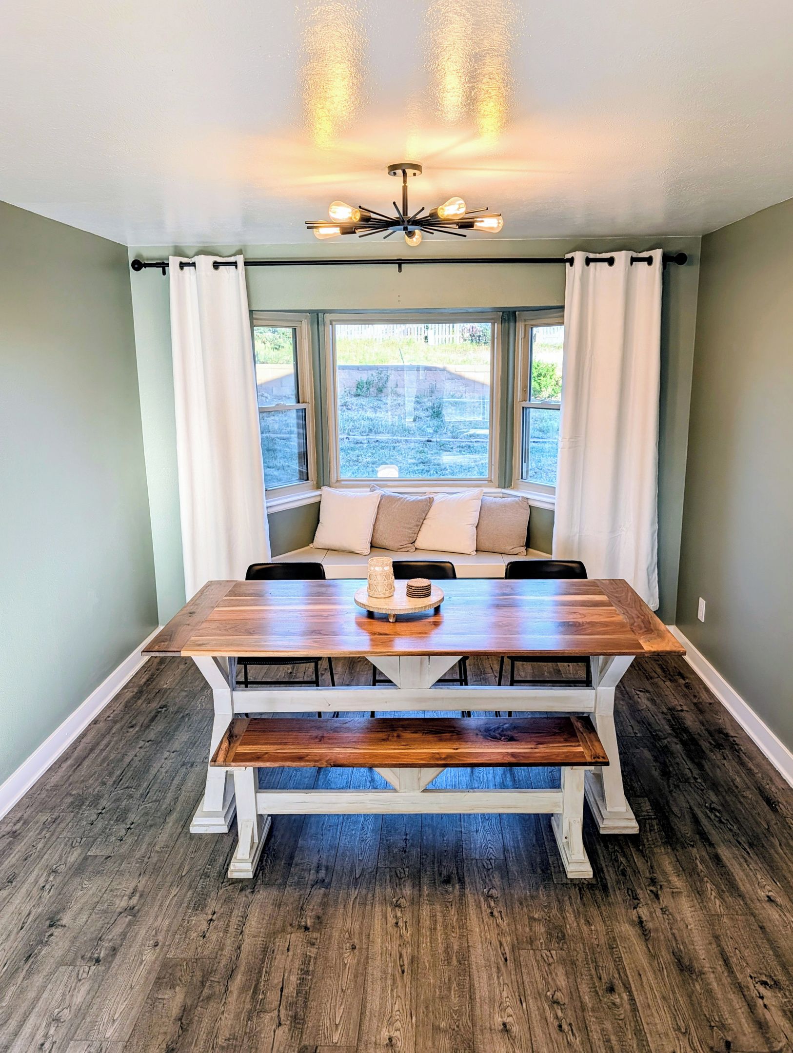 A dining area with a wooden table, benches, and a view through large windows.