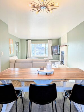 Ein Essbereich mit Holztisch, schwarzen Stühlen, einer Couch, einem Fernseher und einem Kamin.