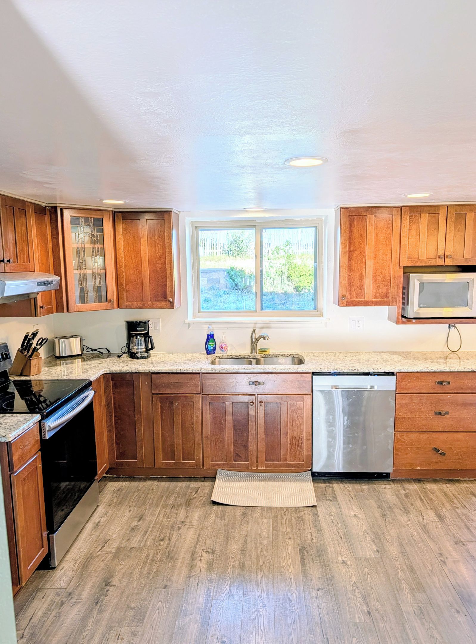 A kitchen with wooden cabinets, a stainless steel dishwasher, a microwave, and a window providing natural light.