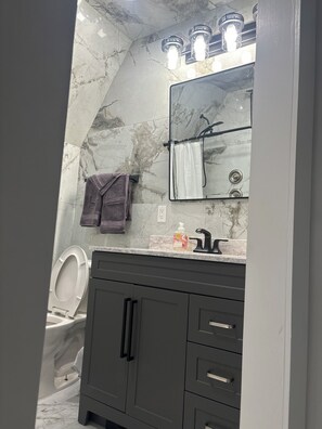A bathroom with a marble wall, a modern vanity, a toilet, and a shower area.
