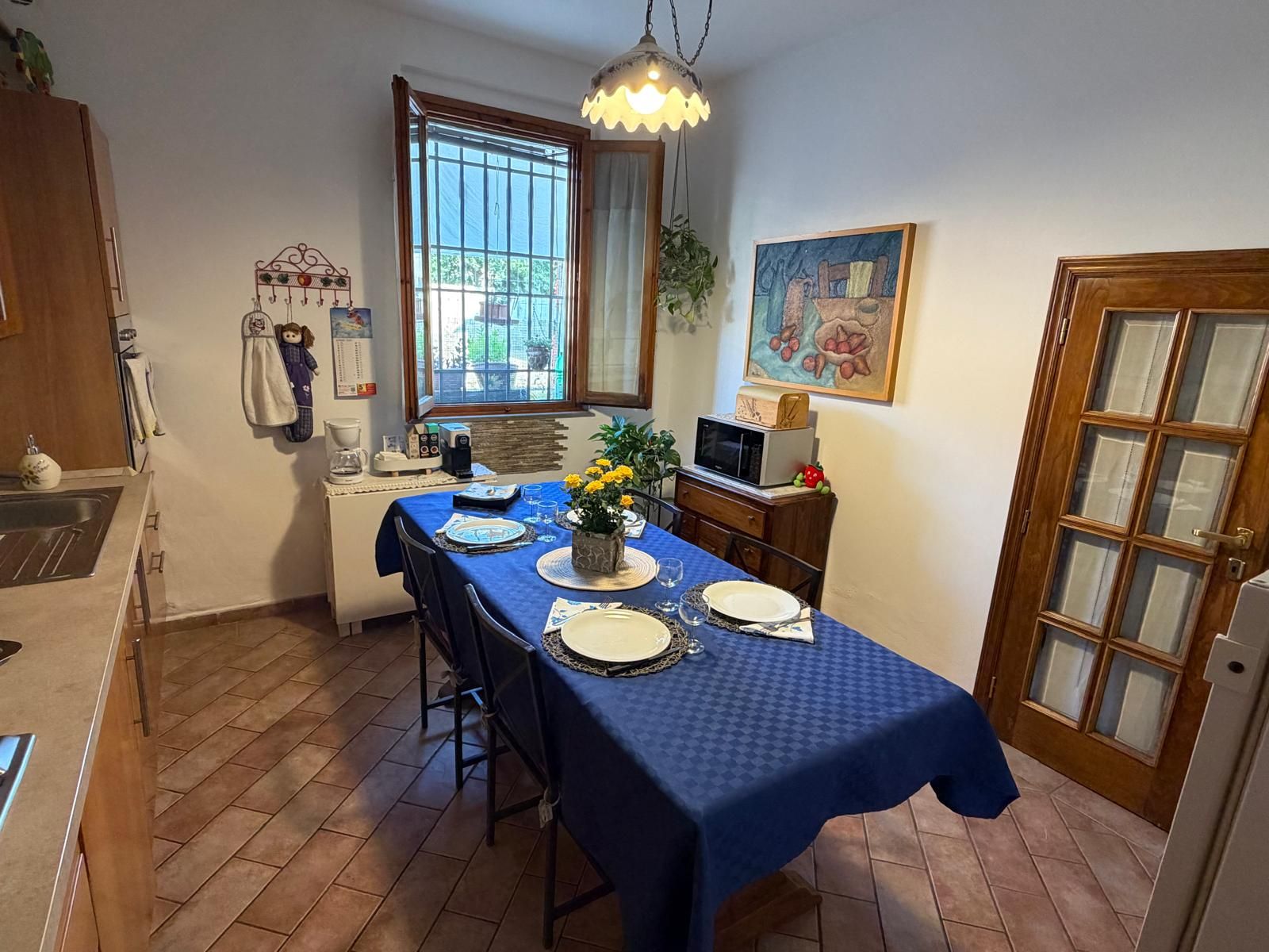 Zona pranzo con tavolo imbandito per quattro persone, una finestra con vista e angolo cottura con forno a microonde.