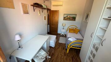 Une pièce de taille modeste comprenant un lit, un bureau, une chaise, une petite table et une étagère avec quelques objets.