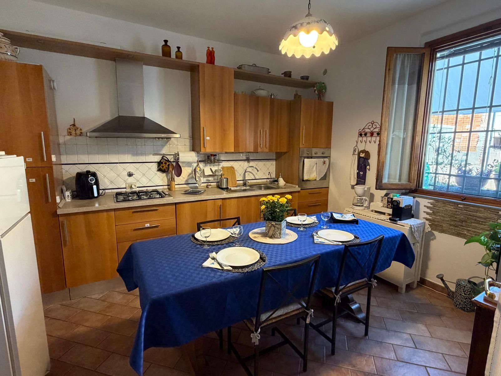 Een keuken met houten kastjes, een gasfornuis en een eettafel voor vier personen, gedekt met blauwe tafelkleden.
