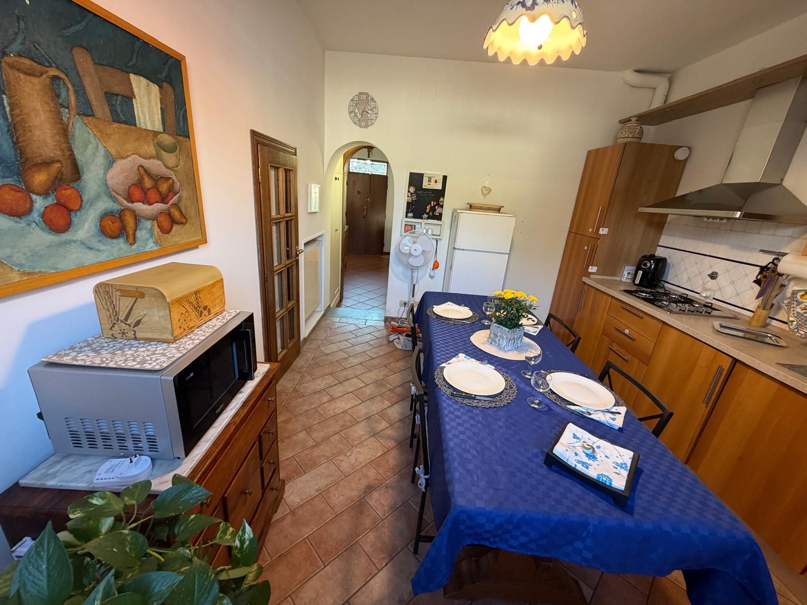 Un coin repas avec une table dressée pour quatre personnes, une cuisine équipée d’appareils modernes et un couloir menant à une autre pièce.