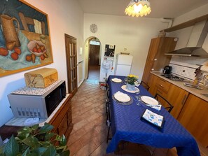 Ein Essbereich mit Tisch für vier Personen, eine Küche mit modernen Geräten und ein Flur, der in einen weiteren Raum führt.