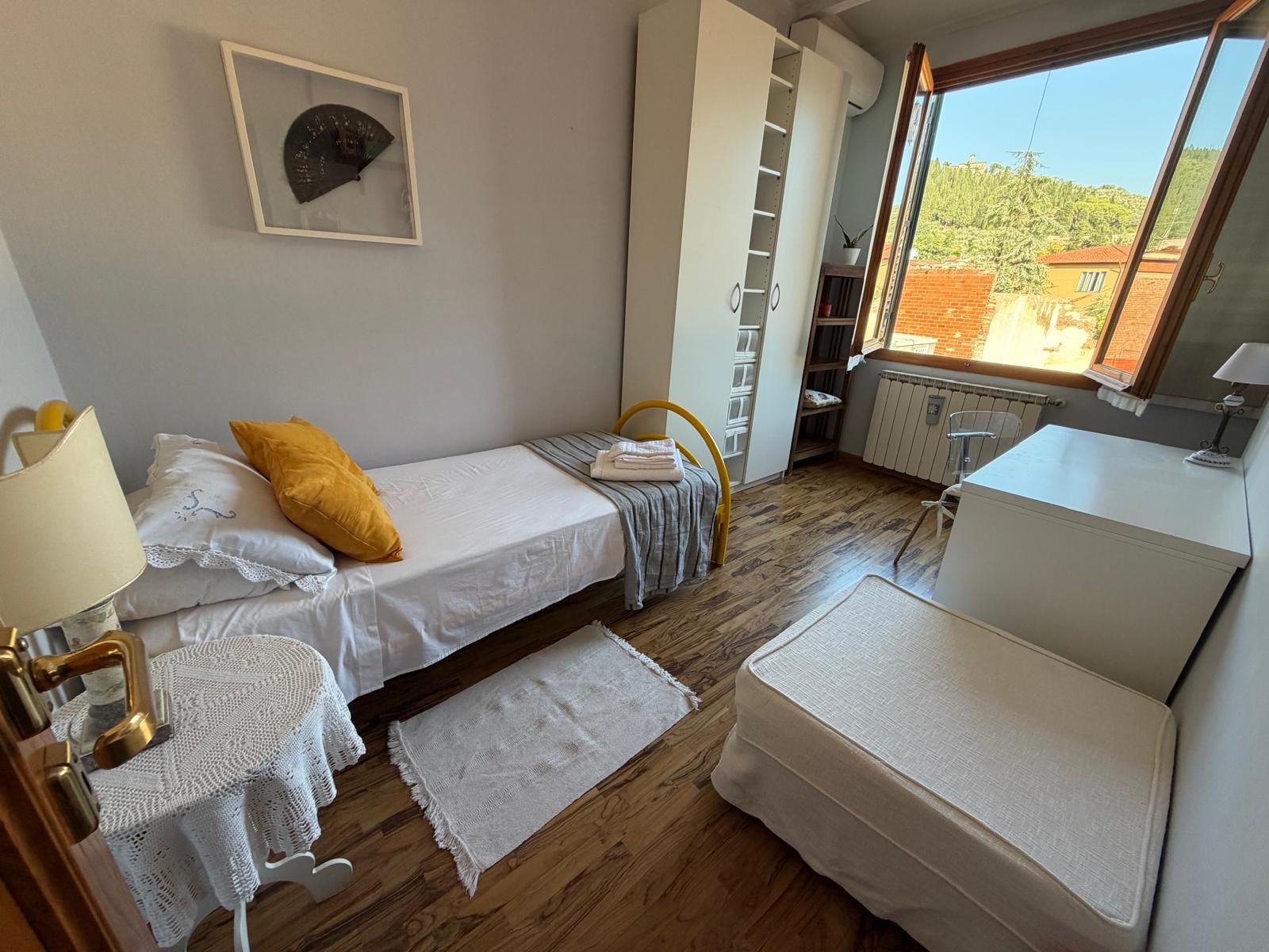 A compact bedroom with a bed, bedside table, lamp, and a view of the outdoors.