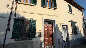 Un bâtiment à deux étages avec une porte marron, des volets verts et un petit porche.