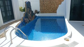 A swimming pool with a mosaic tile design, a metal ladder, and a stone wall backdrop. - Vila Verissimo  (Jericoacoara)