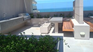 Una terrassa al terrat amb una barbacoa, zona de seients i vista al mar.