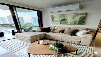 A modern living room with a sectional sofa, a coffee table, and a large window offering a view of the cityscape.