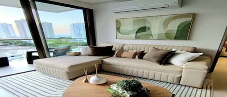 A modern living room with a sectional sofa, a coffee table, and a large window offering a view of the cityscape.