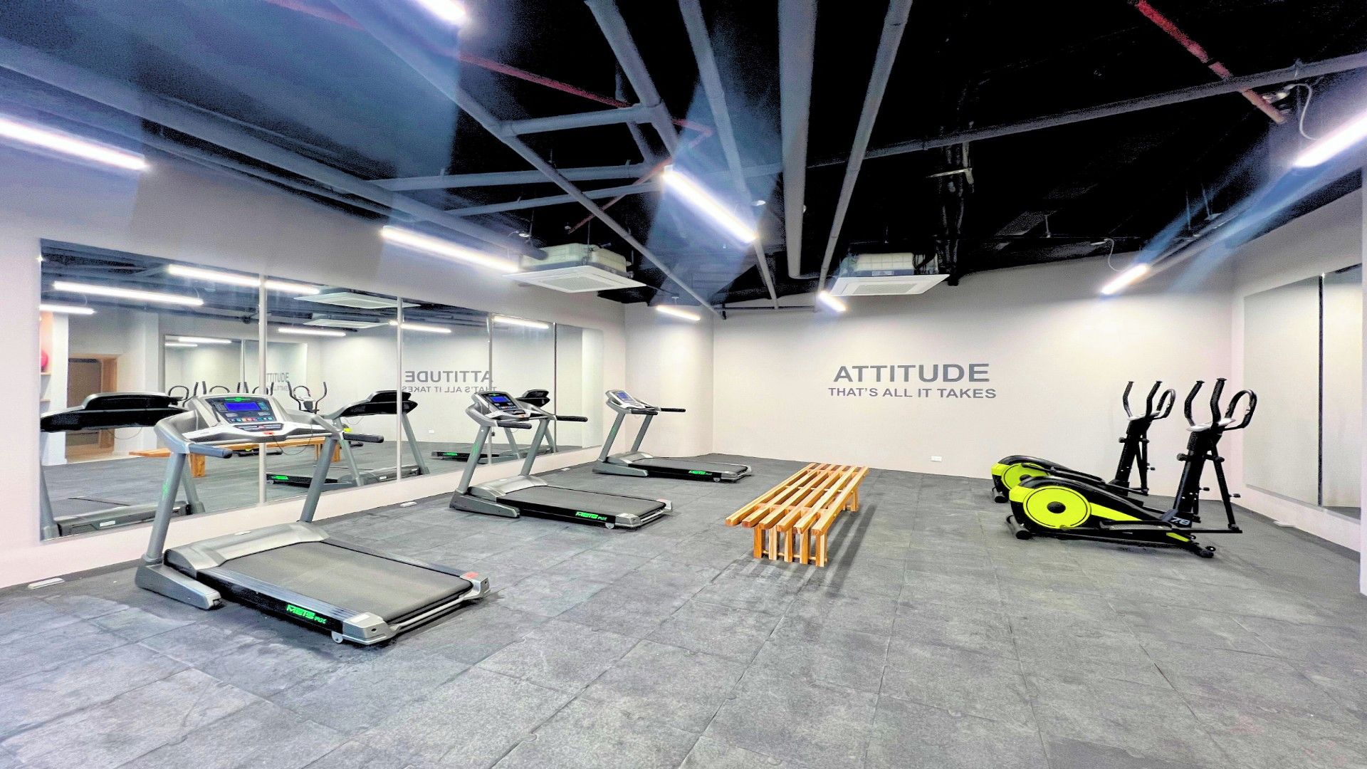 Une salle de sport équipée de tapis de course, de vélos d’appartement et d’un banc en bois.