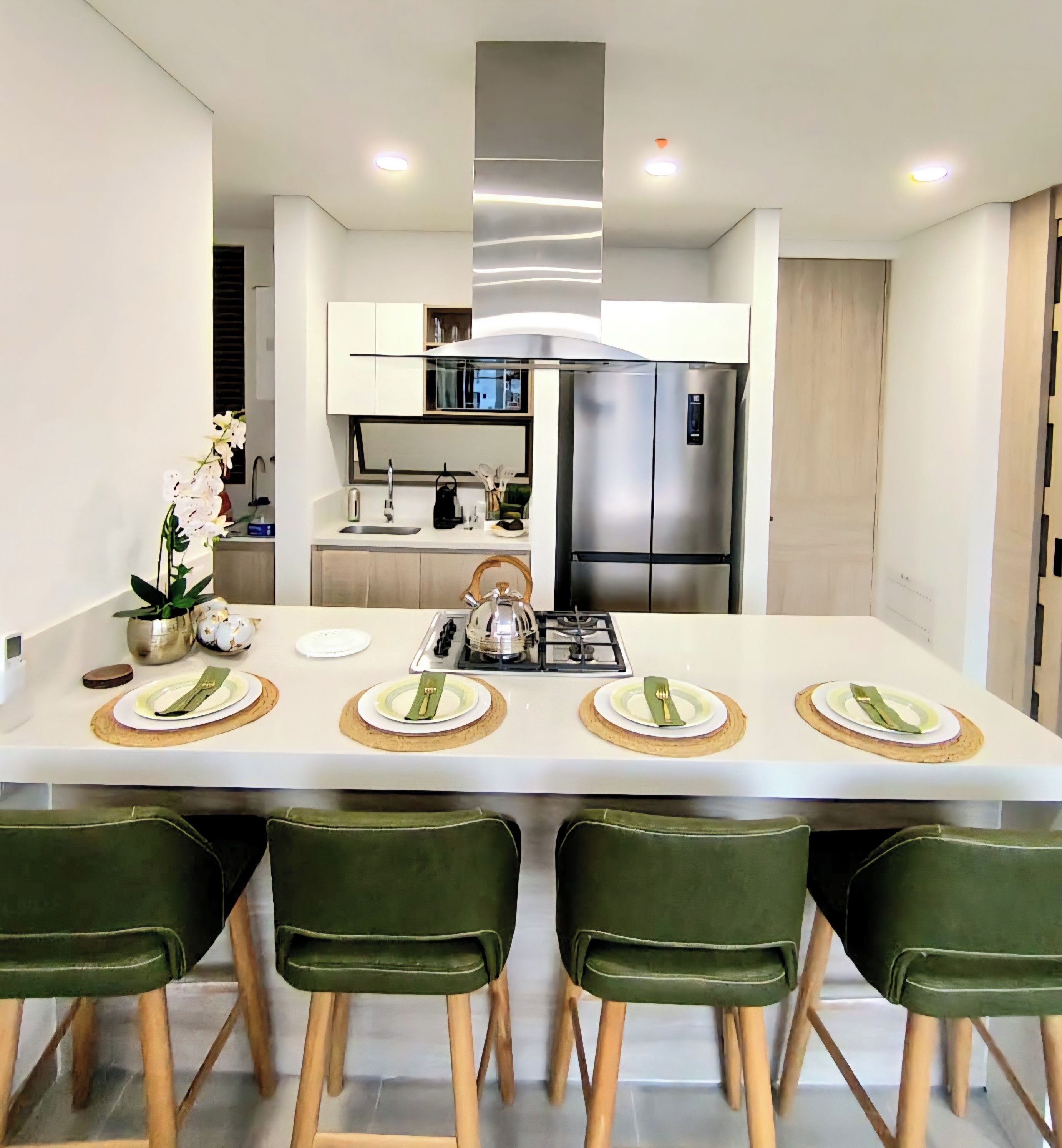 Une cuisine moderne dotée d’un îlot central, d’appareils électroménagers en acier inoxydable et de chaises vertes.