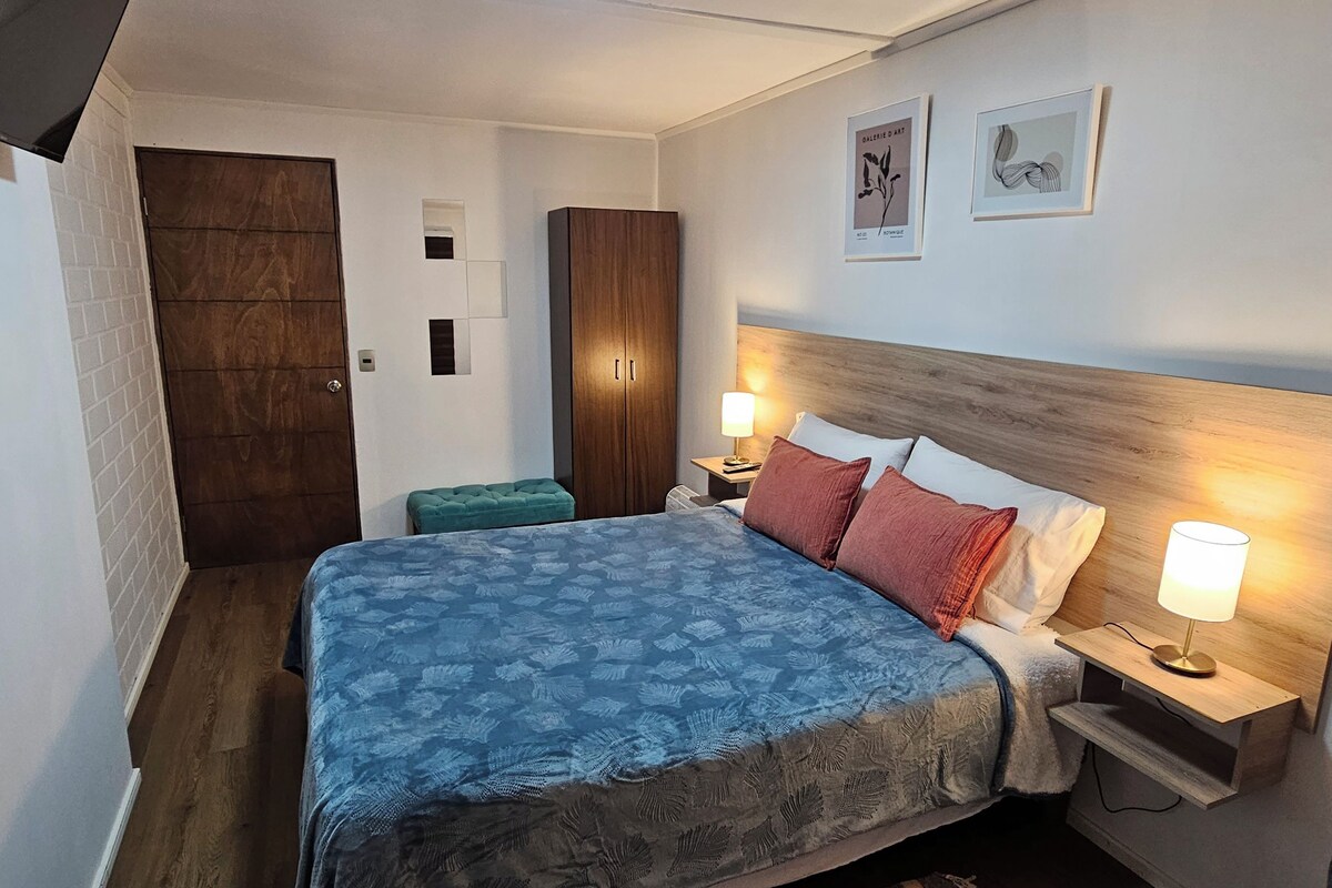 Une chambre d’hôtel comprenant un lit, des tables de chevet, une commode, un banc et des œuvres d’art accrochées au mur.