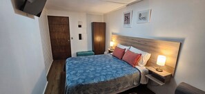 Une chambre d’hôtel comprenant un lit, des tables de chevet, une commode, un banc et des œuvres d’art accrochées au mur.