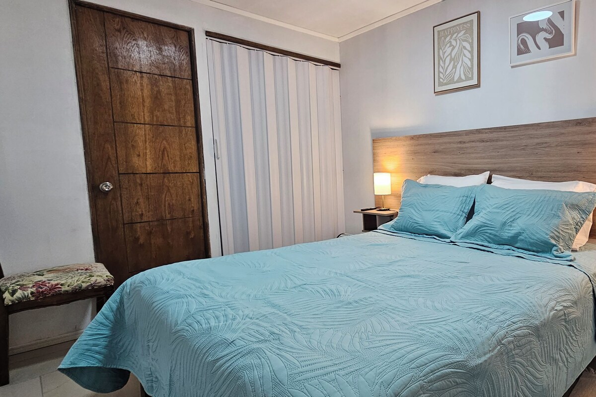 Une chambre à coucher avec un lit, deux lampes de chevet, une tête de lit en bois, une porte et une fenêtre avec des rideaux.
