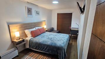 A hotel room with a bed, bedside lamps, a desk, a chair, and a radiator.