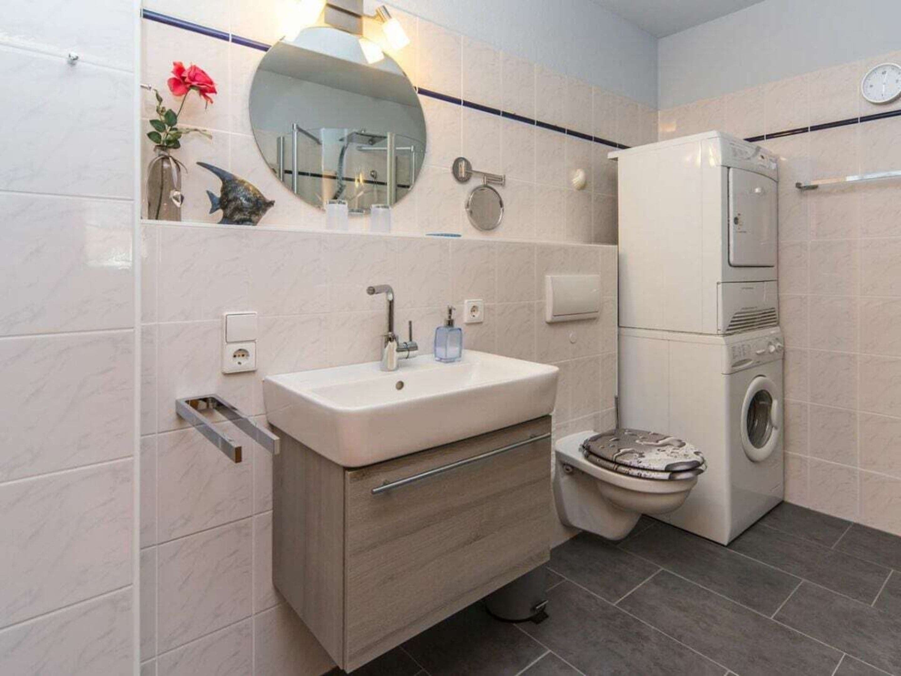 A modern bathroom with a sink, mirror, toilet, and a washing machine.