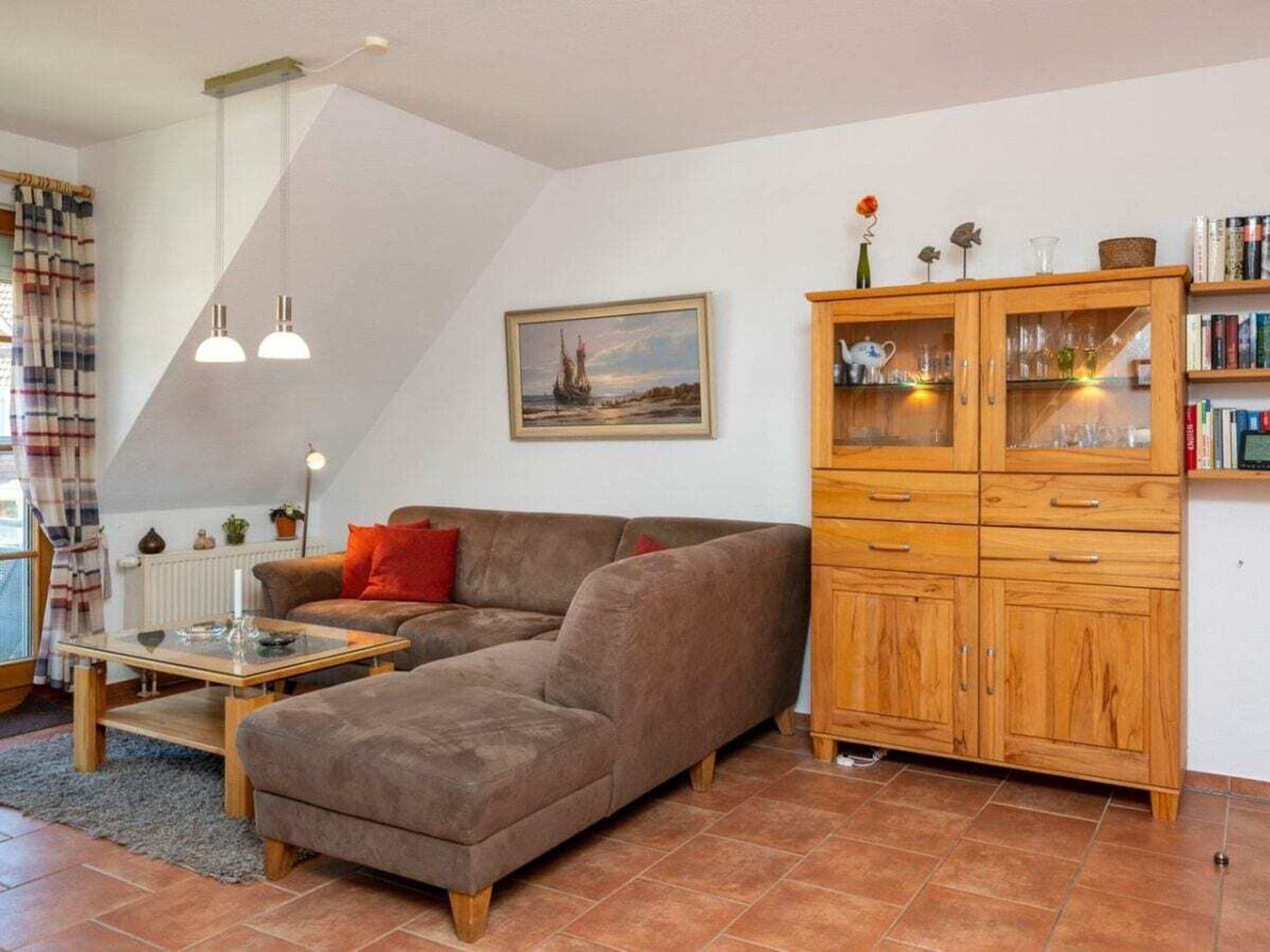 Ein Wohnzimmer mit Ecksofa, einer Holzvitrine, einem Bild an der Wand und einem Fenster mit Vorhängen.