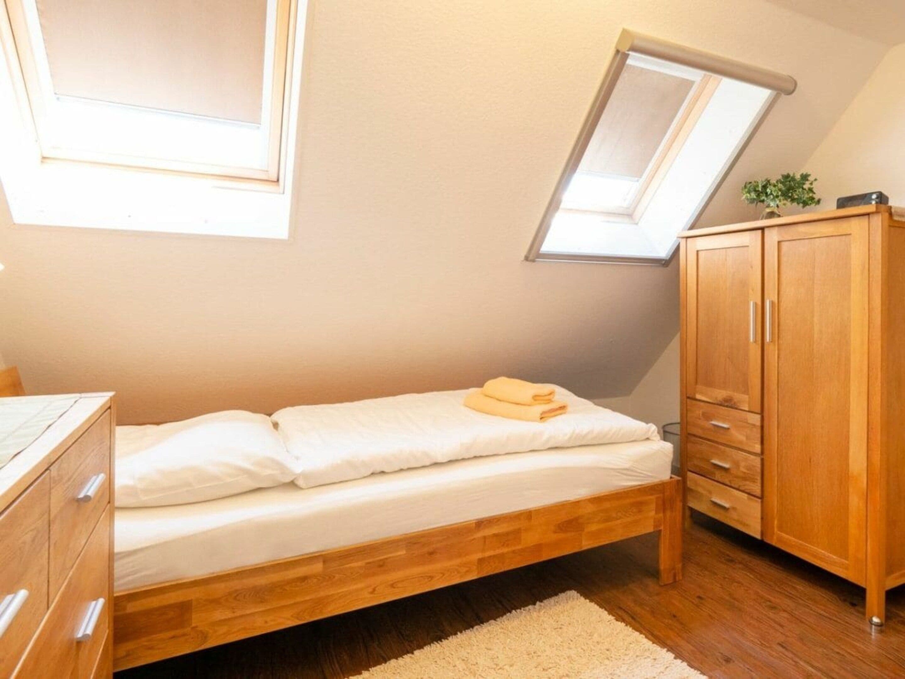 Een slaapkamer met een enkel bed, een houten kledingkast en een dakraam.