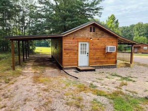 Eine Holzhütte mit überdachter Veranda, einer Tür und einer kleinen Klimaanlage.