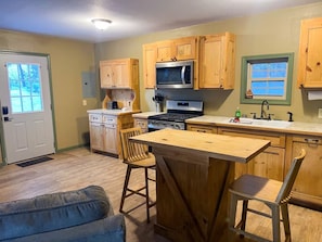A kitchen with wooden cabinets, a microwave, a stove, and a bar area with stools.
