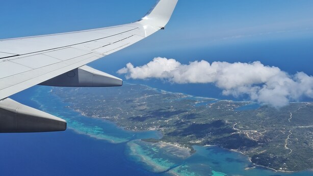 Ala de avión con vista a una costa y aguas azul turquesa.