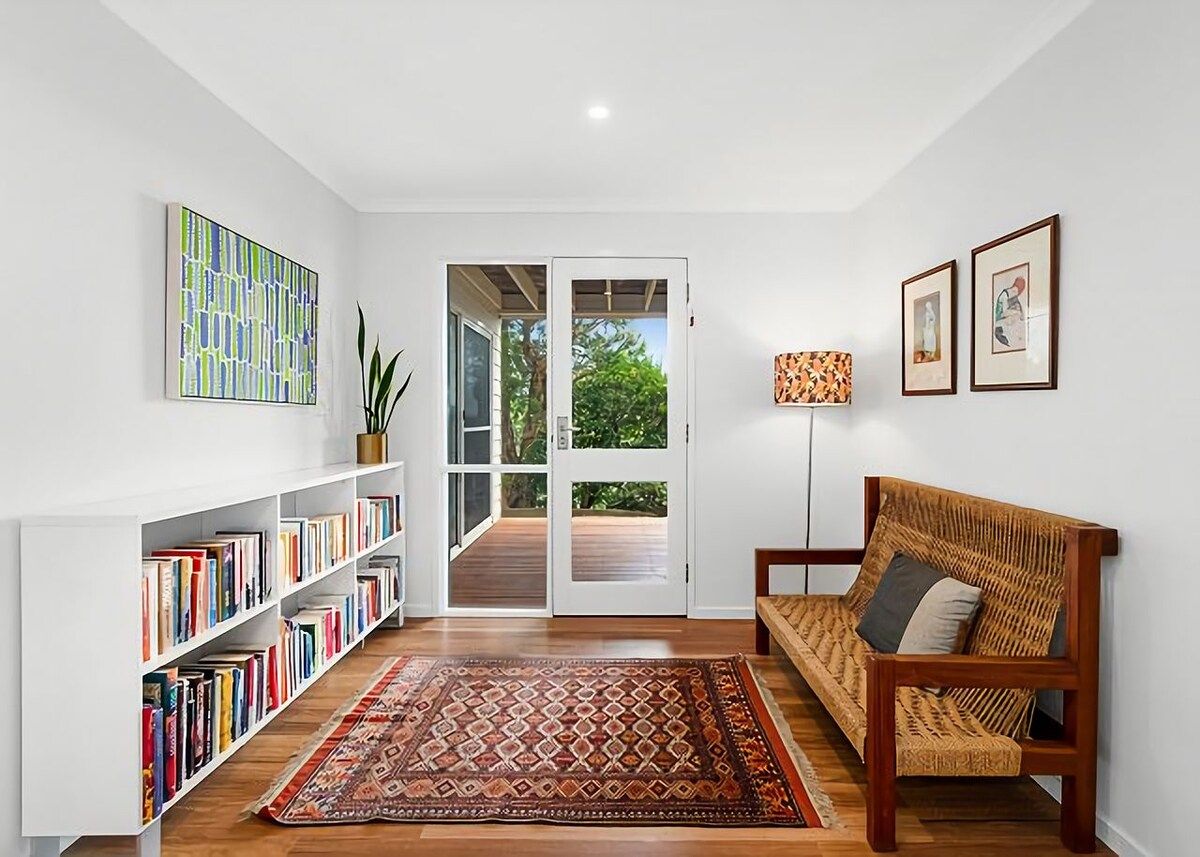 Une pièce avec une bibliothèque, un tapis à motifs, un canapé et une porte donnant sur l’extérieur.