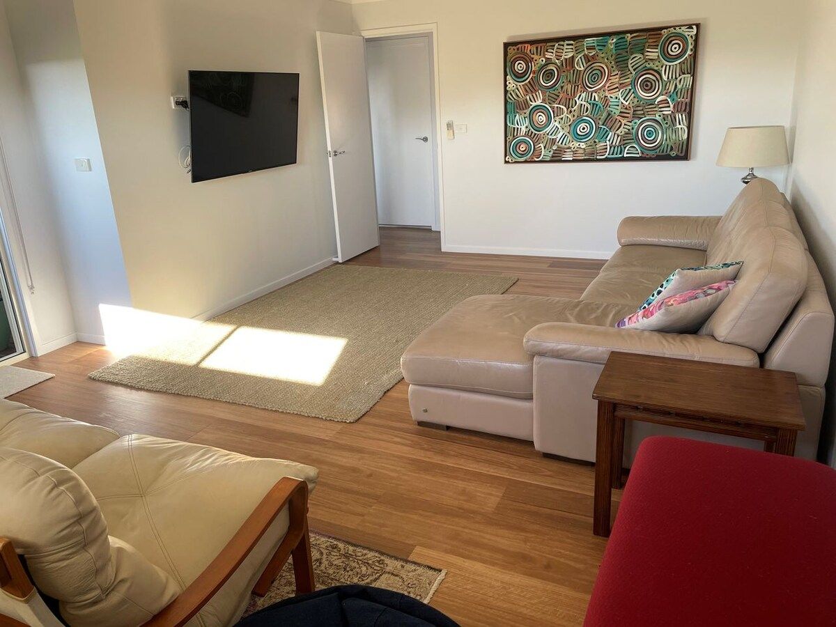A living room with a sofa, a red chair, a wooden table, and a television mounted on the wall.