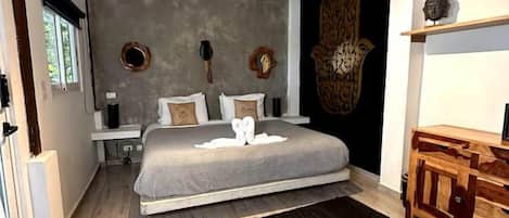 Quarto com cama, mesas de cabeceira, cômoda de madeira, tapete preto e parede decorada.