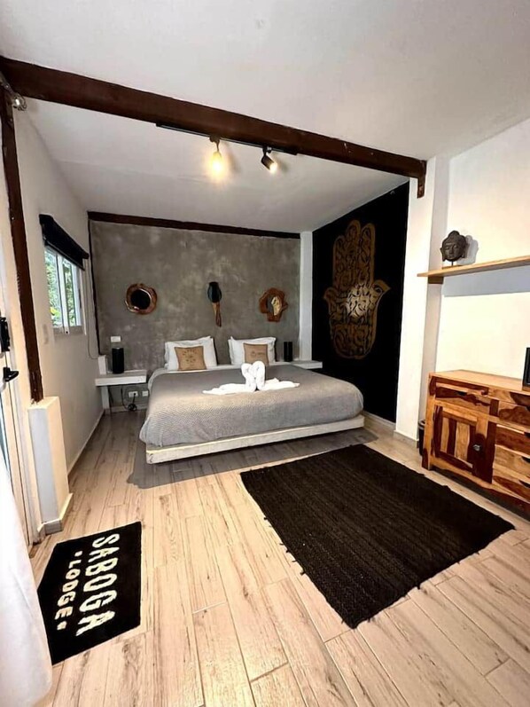 Un dormitorio con cama, mesitas de noche, cómoda de madera, alfombra negra y pared decorada.