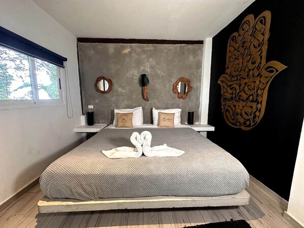 A modern bedroom with a large bed, two bedside tables, and a decorative wall piece.