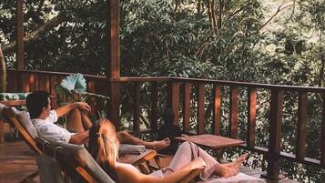 Une terrasse en bois, agrémentée de chaises longues et d’une table, entourée d’une végétation luxuriante.