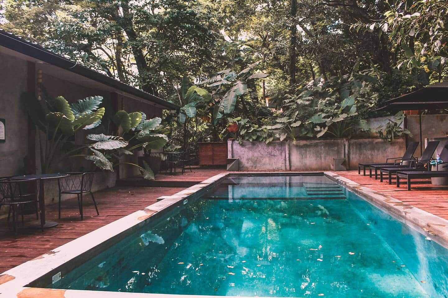 Une piscine rectangulaire entourée d’une terrasse en bois, avec des bancs et des chaises.