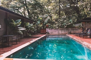 Une piscine rectangulaire entourée d’une terrasse en bois, avec des bancs et des chaises.