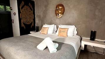 A modern bedroom with a large bed, a headboard with a decorative mask, and a bedside table with a lamp.
