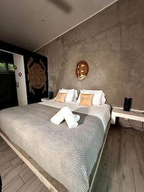 A modern bedroom with a large bed, a headboard with a decorative mask, and a bedside table with a lamp.