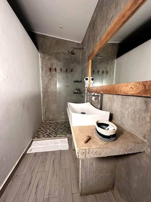 Un baño moderno con lavamanos integrado, zona de ducha y estante de madera.