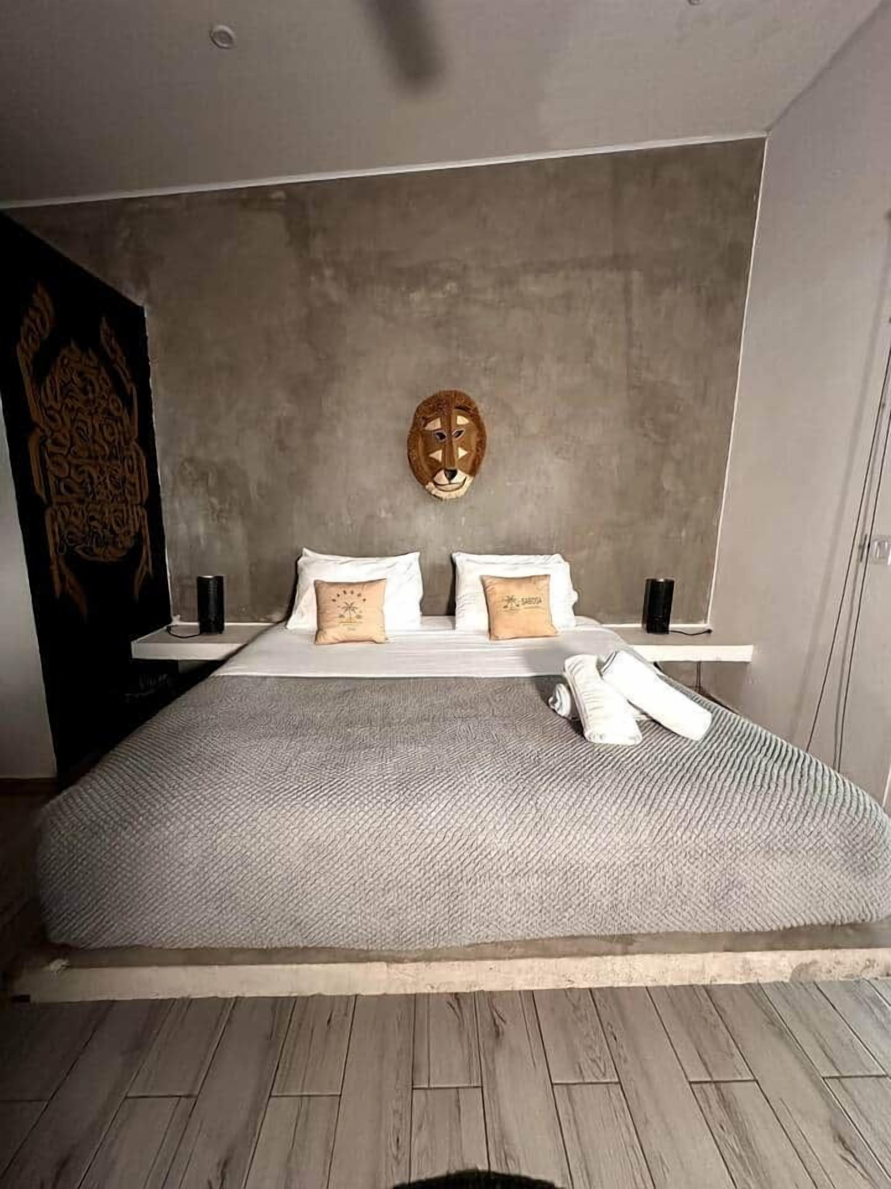 Een moderne slaapkamer met een groot bed, een hoofdbord met een decoratief masker, en een houten vloer.