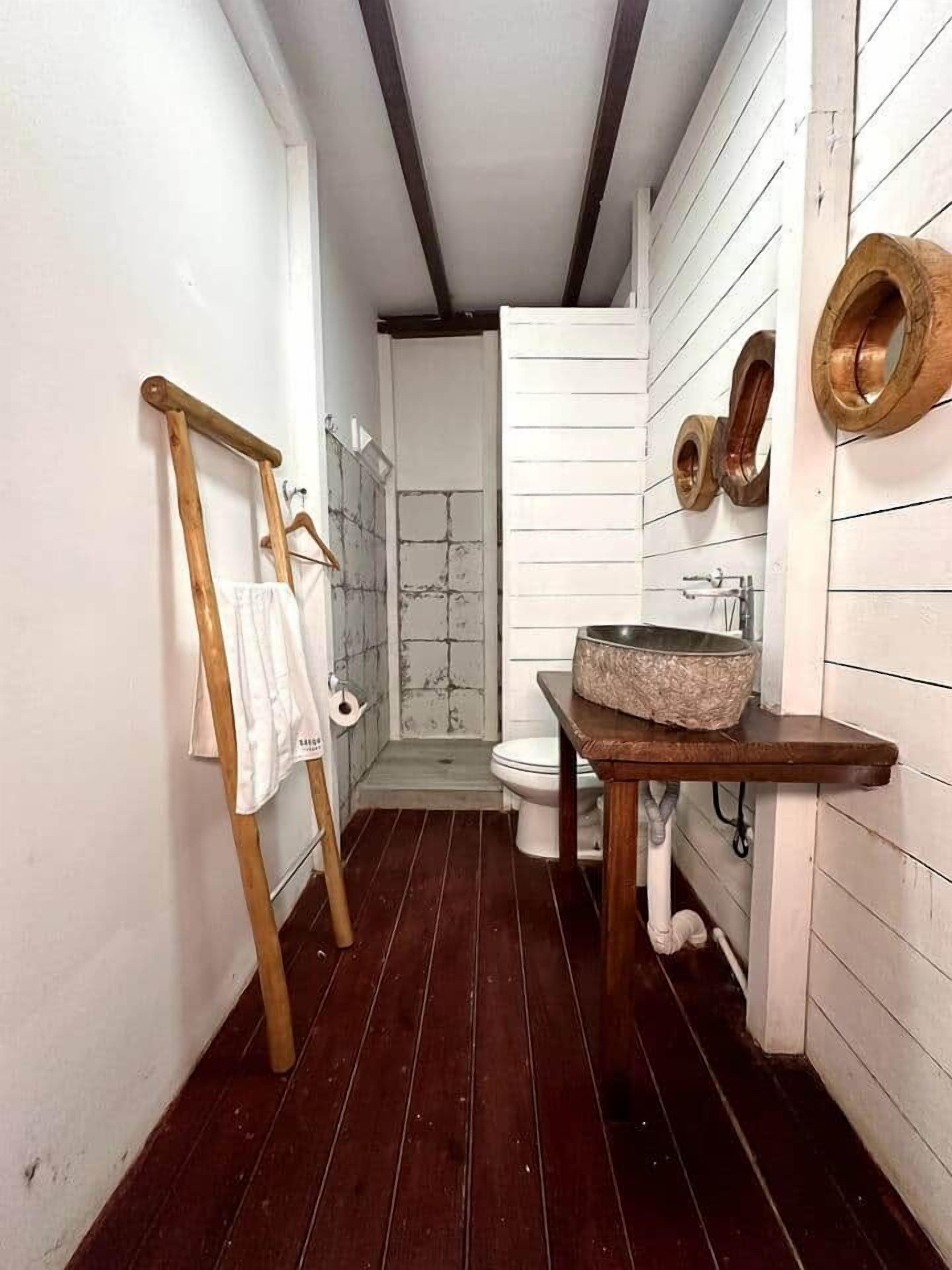 A narrow bathroom with a wooden floor, a white sink with a stone basin, and a wooden towel rack.