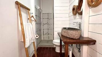A narrow bathroom with a wooden floor, a white sink with a stone basin, and a wooden towel rack.