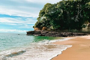Un paisaje costero con una playa arenosa, un acantilado rocoso y un mar tranquilo.