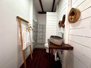 Un baño estrecho con una escalera de madera, un lavamanos blanco con cuenca de piedra y un inodoro.