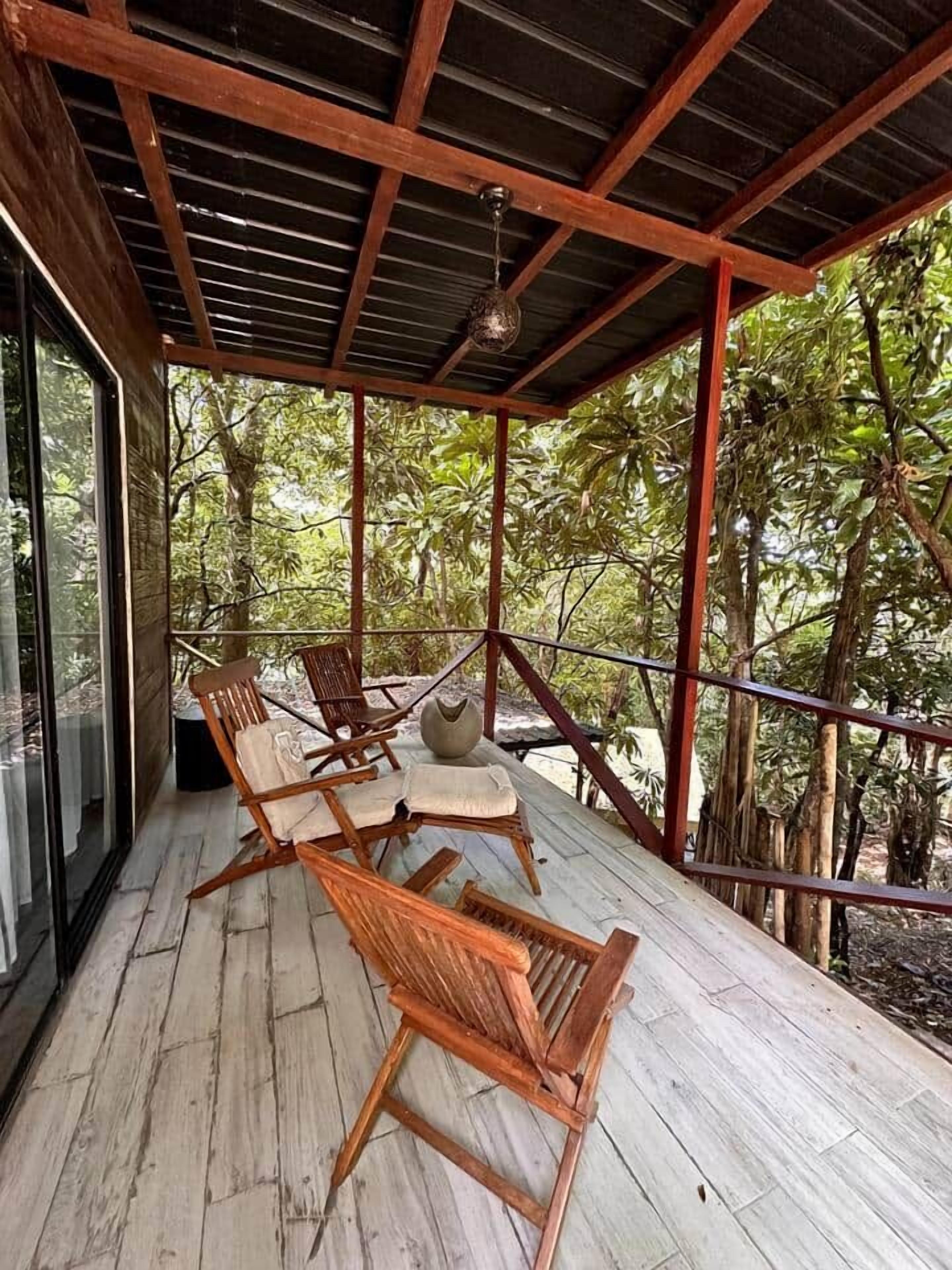 Un espacio de estar al aire libre techado, con mobiliario de madera y pared de vidrio.