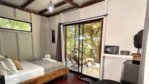Un dormitorio con cama, una mesita, una silla y vistas al exterior a través de un ventanal.