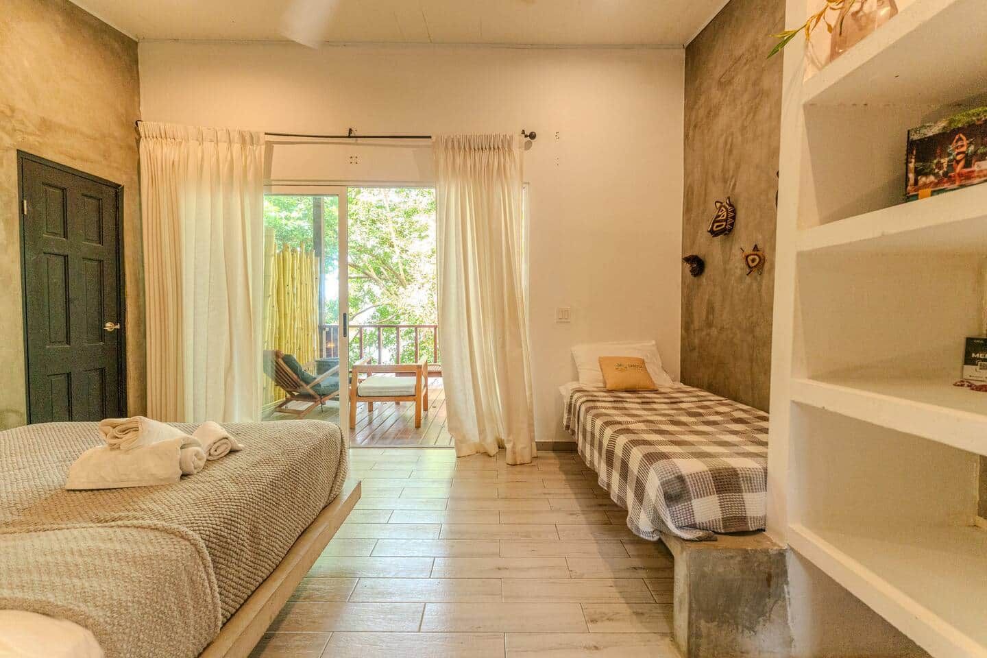 Een kamer met een bed, een klein tafeltje, een stoel, een plank en uitzicht op het buiten.