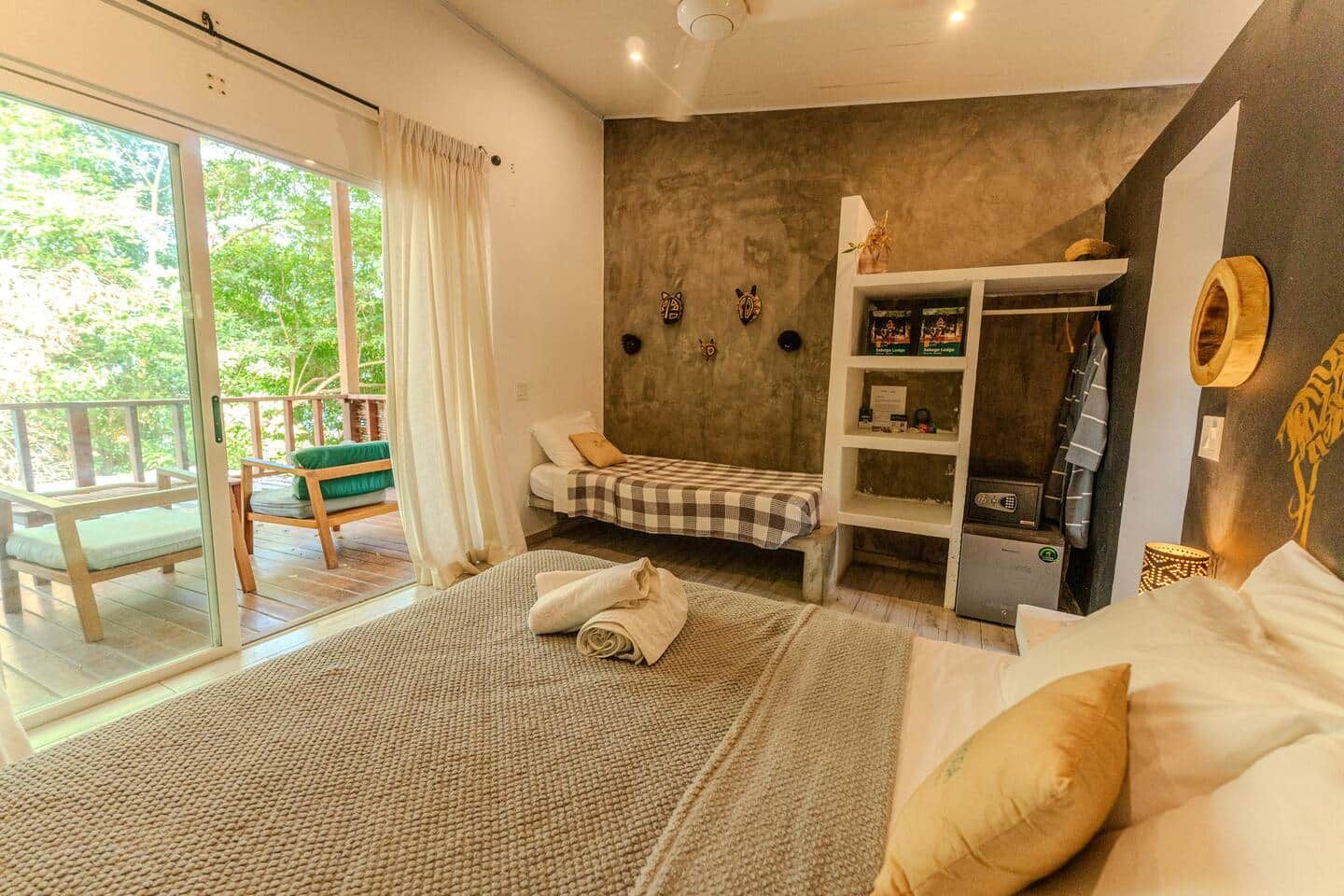 Una habitación con cama, sofá, una mesita, una estantería y un ventanal corredero que da a un espacio exterior.
