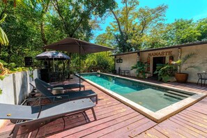 A swimming pool with lounge chairs and an umbrella, surrounded by greenery and a building labeled 'MAMASTE.'